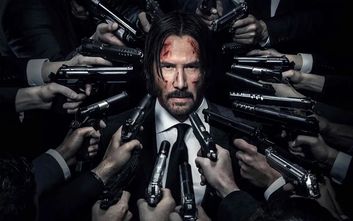 Silahların çevrelediği yaralı John Wick.